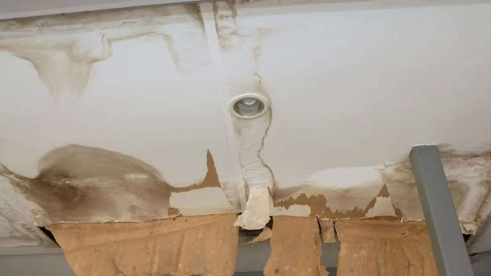 Water-stained ceiling around a light fixture with damaged drywall